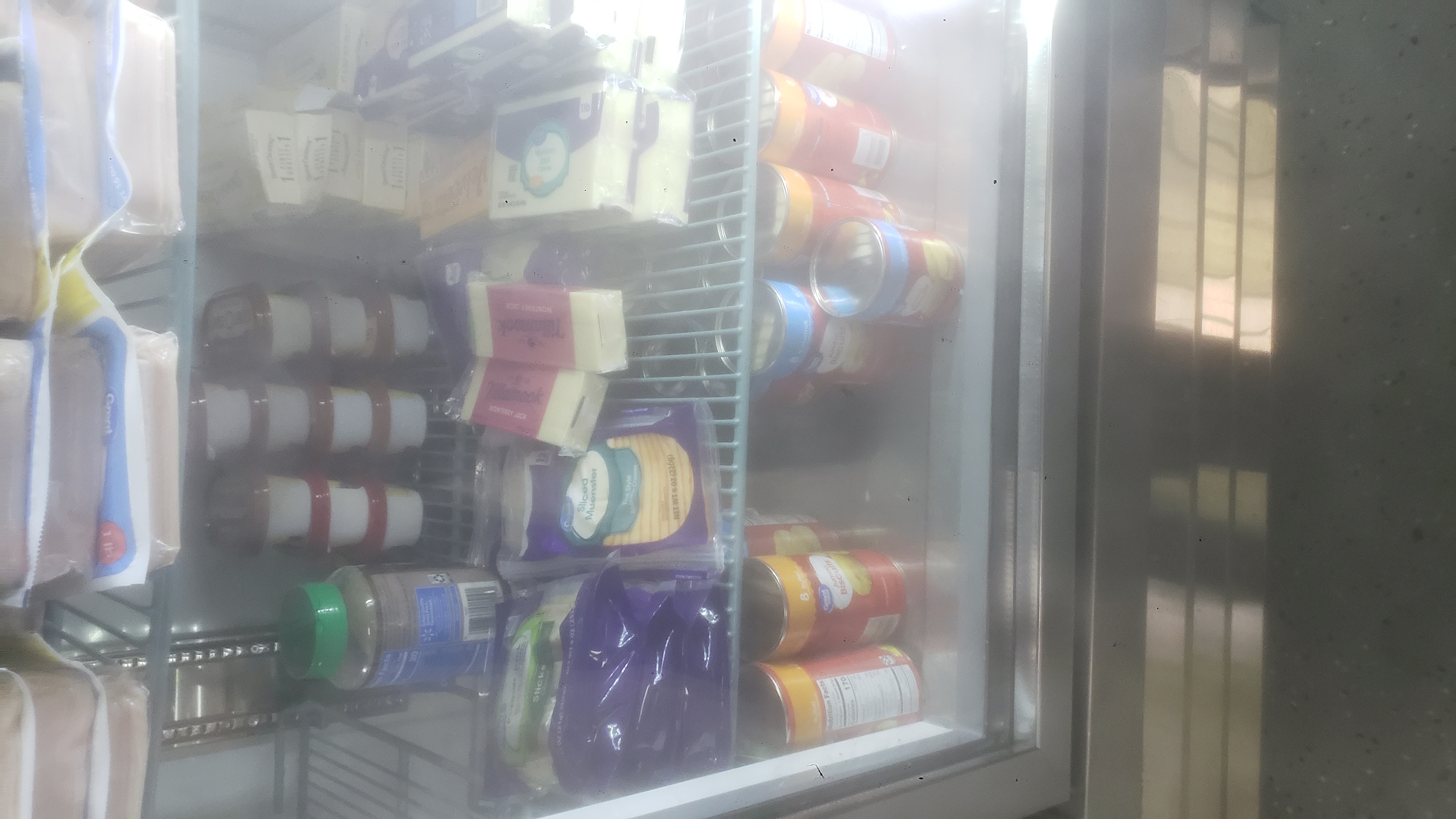 Cans of biscuits, blocks of cheese, pack of sliced cheese, packs of cheese sticks, boxes, and containers of butter in a fridge.